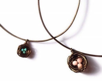 May include: Two delicate necklaces with wire bird nests as pendants. One nest contains three turquoise blue beads, the other contains three pink beads.