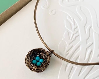May include: A delicate gold necklace with a wire-wrapped bird's nest pendant containing turquoise blue beads.