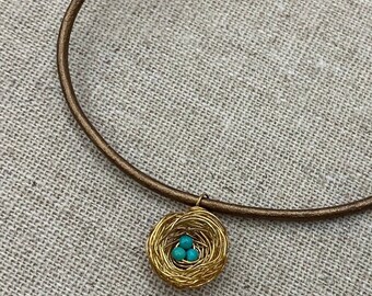 Mini bird nest pendant necklace with blue eggs made of Kingman turquoise from Arizona. Gold tone brass and leather cord.