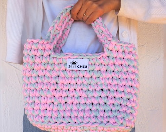 May include: A pink and green crocheted tote bag with a white label that says "STITCHES" with a sun graphic.