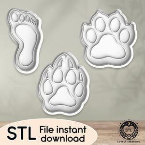Puede incluir: Tres cortadores de galletas impresos en 3D, una huella de pata y dos huellas de patas diferentes. Los cortadores de galletas son blancos y tienen un acabado liso. El texto "STL File instant download" está en la parte inferior de la imagen.