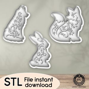 May include: Three white cookie cutters in the shapes of a dog, a fox, and a rabbit, each with floral designs. The image includes the text "STL File instant download" and a logo.