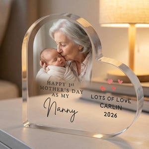Puede incluir: Marco de fotos acr&iacute;lico en forma de coraz&oacute;n con una foto de una abuela besando a un beb&eacute;. El marco incluye el texto "Happy 1st Mother's Day as my Nanny" y "Lots of Love, Carlin 2026".