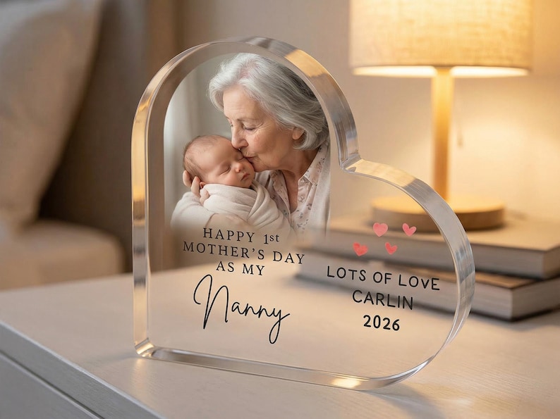 Puede incluir: Marco de fotos acr&iacute;lico en forma de coraz&oacute;n con una foto de una abuela besando a un beb&eacute;. El marco incluye el texto "Happy 1st Mother's Day as my Nanny" y "Lots of Love, Carlin 2026".