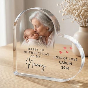 Puede incluir: Marco de fotos acr&iacute;lico en forma de coraz&oacute;n con una foto de una abuela besando a un beb&eacute;. El marco tiene el texto: "Happy 1st Mother's Day as my Nanny. Lots of Love, Carlin 2026."