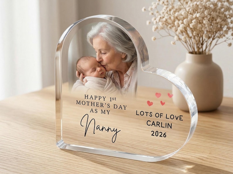 Puede incluir: Marco de fotos acr&iacute;lico en forma de coraz&oacute;n con una foto de una abuela besando a un beb&eacute;. El marco tiene el texto: "Happy 1st Mother's Day as my Nanny. Lots of Love, Carlin 2026."