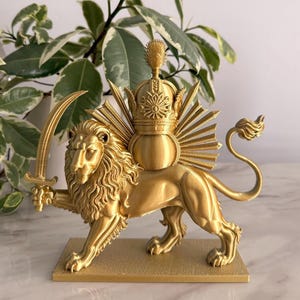 Puede incluir: Escultura dorada de un león sosteniendo una espada, con un diseño de corona y rayos de sol en la espalda. El león está sobre una base rectangular. La escultura es probablemente un objeto decorativo.