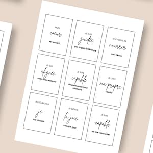 Könnte beinhalten: Weiße Karten mit schwarzem Text im minimalistischen Stil. Jede Karte enthält einen Satz auf Französisch, wie "Je suis capable" und "Je choisis ce qui m'élève". Die Karten sind auf einer hellen Oberfläche angeordnet.