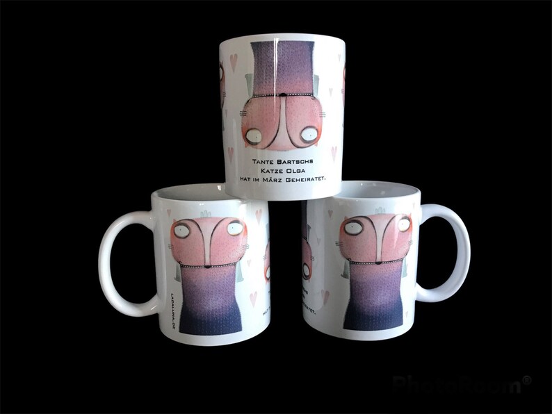 May include: Three white ceramic mugs with a cartoon illustration of a pink cat wearing a purple dress. The text on the mug reads "Tante Bartsch Katze Olga hat im M&auml;rz geheiratet."