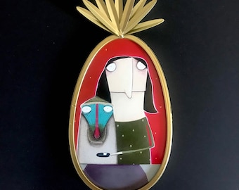 May include: A framed illustration of a woman with long black hair and a creature with a long nose and large eyes. The woman is wearing a green shirt with white dots and the creature is wearing a blue and green hat. The frame is gold and has a decorative design at the top.