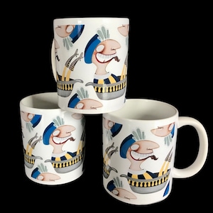 May include: Three white ceramic mugs with a repeating cartoon design. The design features a smiling character with a blue hat, yellow and black striped shirt, and a tongue sticking out. The character is in a cooking pot.