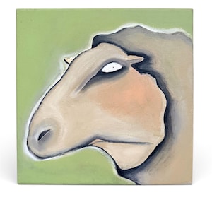 May include: A square canvas artwork depicting a sheep's head in profile. The sheep is painted in beige, tan, and grey, with a light peach face and a single, wide-eyed stare. The background is a soft, muted green.