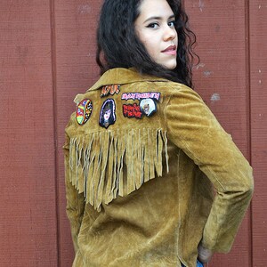 May include: A brown suede jacket with fringe on the back. The jacket has several band patches sewn on the back, including "AC/DC", "Iron Maiden", and "Ramones".