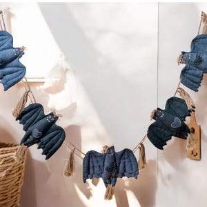 Pode incluir: Guirlanda decorativa de morcegos de tecido em tons de azul e preto, pendurados em fio natural. Cada morcego tem asas detalhadas e um coração decorativo. Ideal para o Halloween ou festas temáticas.