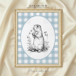 May include: Framed art print featuring a detailed black and white illustration of a prairie dog holding a flower. The artwork is set against a light blue gingham pattern within a white oval, framed in gold. Text at the top reads "ALEX ART HUB" and at the bottom "Bring the gallery home".