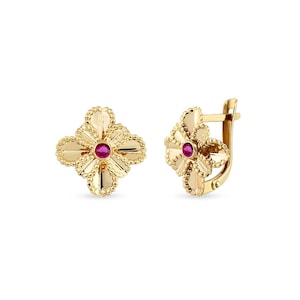 May include: A pair of gold-colored earrings. Each earring features a four-leaf clover design with a small, round, red gemstone in the center. The earrings have a textured surface and a lever back closure.
