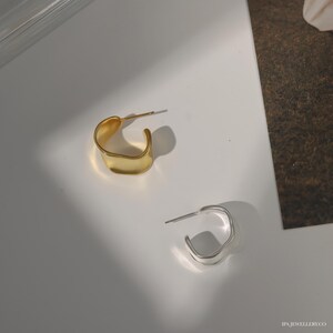 May include: Two pairs of earrings, one gold and one silver, with a unique, asymmetrical, wavy design. The earrings are simple and modern.