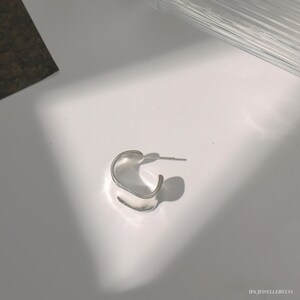 May include: A silver hoop earring with a unique, slightly curved, rectangular shape.