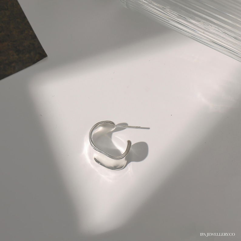 May include: A silver hoop earring with a unique, slightly curved, rectangular shape.