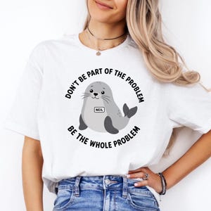 Könnte beinhalten: Ein weißes Kurzarm-T-Shirt mit einer Grafik eines grauen Seehunds, der ein Namensschild mit der Aufschrift NEIL trägt. Der Text um den Seehund lautet DON'T BE PART OF THE PROBLEM BE THE WHOLE PROBLEM in schwarzen Großbuchstaben. Kombiniert mit einer blauen Jeans.