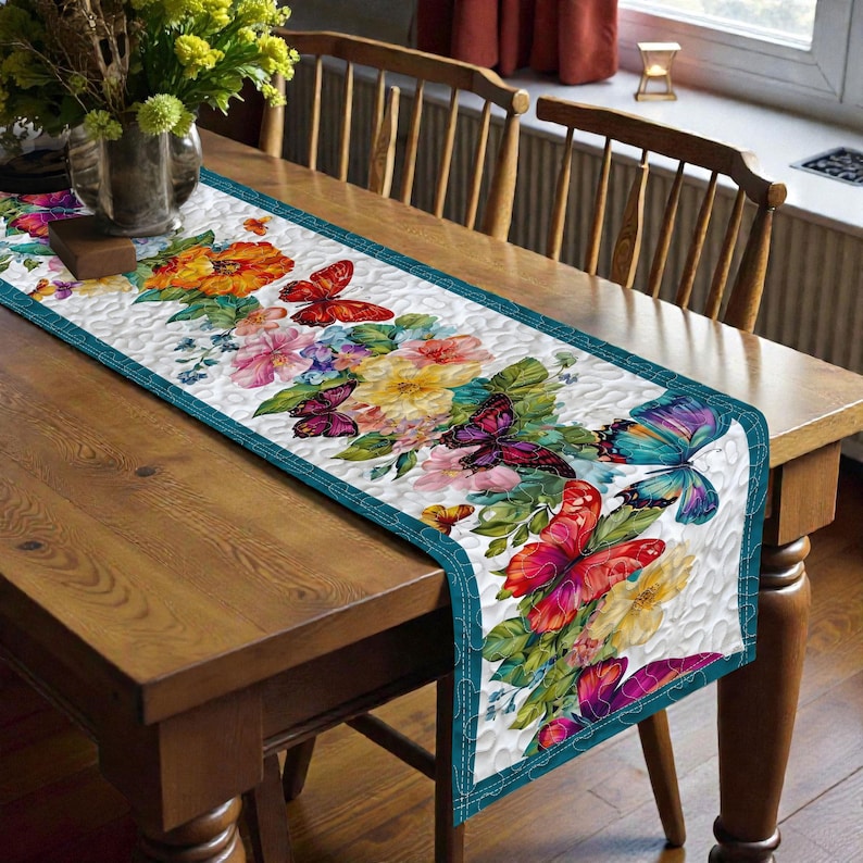 May include: A rectangular table runner with a white background and a floral and butterfly design. The runner features a teal border and is decorated with colorful flowers and butterflies in shades of red, orange, pink, yellow, and blue.