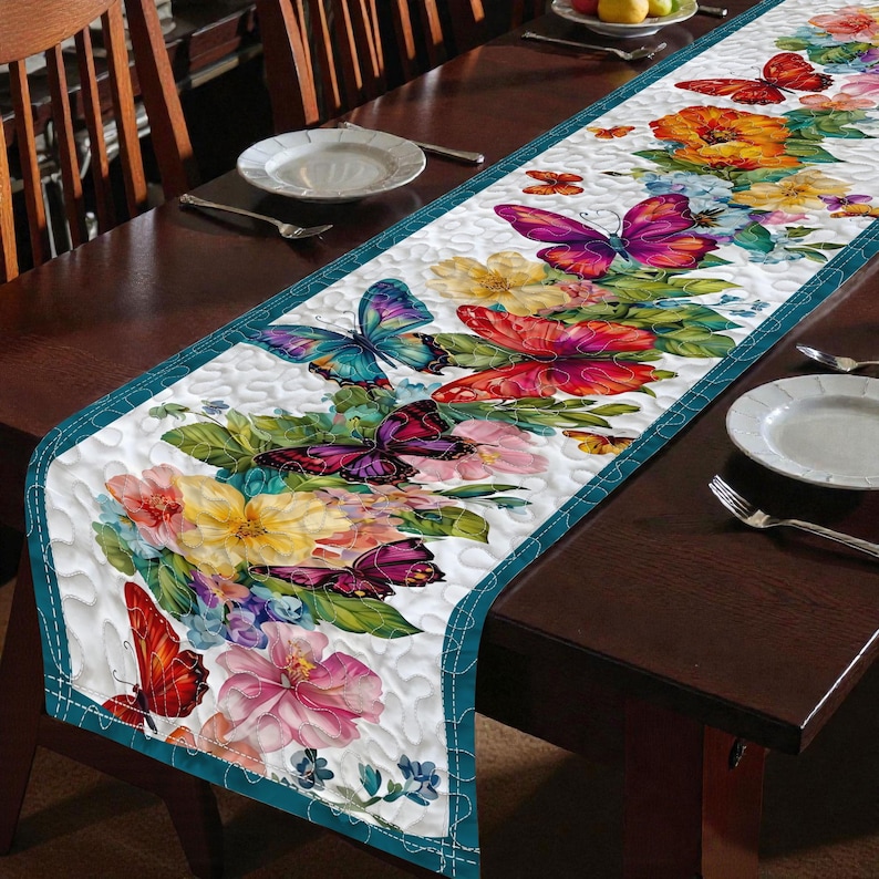 May include: A white table runner with a floral and butterfly design. The runner features a teal border and is decorated with colorful flowers and butterflies in shades of red, pink, yellow, and purple. The runner is placed on a dark brown wooden table.