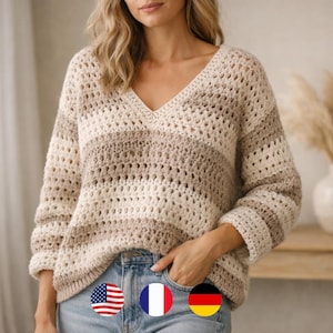 May include: A beige and brown striped crochet sweater with a V-neck. The sweater has long sleeves and a loose fit. The model is wearing blue jeans. The sweater is a cozy and stylish garment.