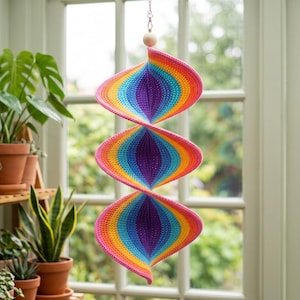 May include: A hanging spiral wind spinner featuring a vibrant crochet pattern with concentric layers of pink, orange, yellow, green, blue, and purple. The structure is suspended by a silver chain and topped with a single natural wooden bead.