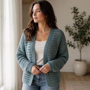 Könnte beinhalten: Hellblauer, offener Strickcardigan mit langen Ärmeln. Der Cardigan hat ein lockeres, offenes Webmuster. Das Model trägt ein weißes Tanktop und blaue Jeans. Ein bequemes und stilvolles Kleidungsstück zum Überziehen.
