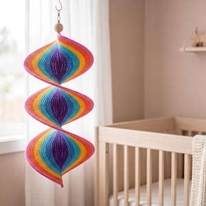 May include: A hanging spiral mobile featuring three interconnected, rounded, crochet-knit sections in a vibrant rainbow gradient of purple, blue, teal, yellow, orange, and pink, suspended from a single wooden bead and a metal hook.