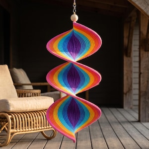 May include: A hanging spiral wind spinner crafted from crocheted yarn in a vibrant rainbow gradient. The structure features three distinct, interconnected conical sections transitioning through colors of pink, orange, yellow, green, blue, and purple.