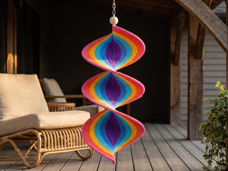May include: A hanging spiral wind spinner crafted from crocheted yarn in a vibrant rainbow gradient. The structure features three distinct, interconnected conical sections transitioning through colors of pink, orange, yellow, green, blue, and purple.