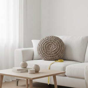 Puede incluir: Un sal&oacute;n de tonos neutros con un sof&aacute; blanco y un gran coj&iacute;n redondo beige tejido. Una mesa de centro de madera con jarrones decorativos y libros. Una cinta m&eacute;trica amarilla descansa sobre el sof&aacute;.