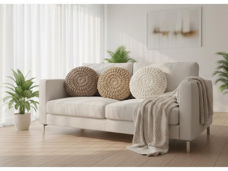 Puede incluir: Un sof&aacute; color crema con tres cojines redondos y texturizados en tonos marr&oacute;n y blanco. Una manta a juego est&aacute; sobre el brazo. Plantas en macetas y una obra de arte abstracta completan la escena de la sala de estar.