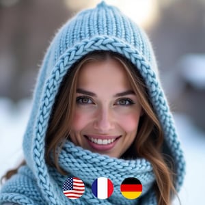 Könnte beinhalten: Ein hellblaues Strickhauben- und Schal-Set. Die Kapuze hat einen dicken, geflochtenen Besatz und einen passenden Schal. Die Frau lächelt, mit langen braunen Haaren und rosigen Wangen. Der Hintergrund ist eine verschneite Winterszene.