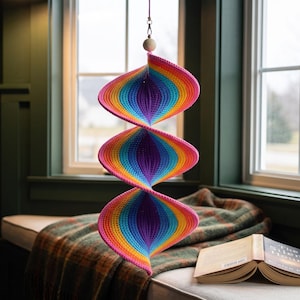 May include: A hanging spiral decoration featuring a vibrant crochet pattern with repeating bands of pink, orange, yellow, light blue, and dark purple. The structure consists of three connected, twisted sections suspended from a single white wooden bead.