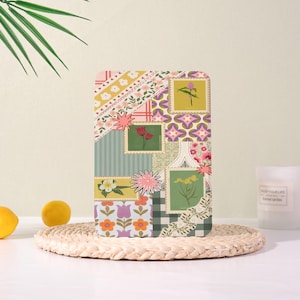 Può includere: Un oggetto rettangolare decorativo con un design patchwork con francobolli floreali, strisce e motivi geometrici nei toni del giallo, rosa, verde e viola. L'oggetto è appoggiato su un tappetino rotondo intrecciato.