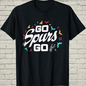 May include: Black t-shirt with the words "GO Spurs GO" in white, with colorful geometric shapes. The San Antonio Spurs logo is also featured. A casual tee for basketball fans.