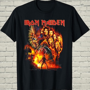 May include: Black t-shirt featuring the band name "Iron Maiden" in red block letters. The graphic includes a fiery image of the band members, a skeletal figure, and a burning building. The design is a vibrant mix of red, orange, and yellow.