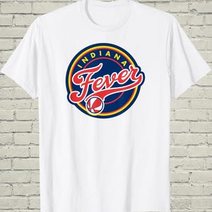 May include: White t-shirt featuring the Indiana Fever logo. The logo is a circular design with the word "Indiana" in a blue ring, and "Fever" in red script. A basketball graphic is at the bottom.