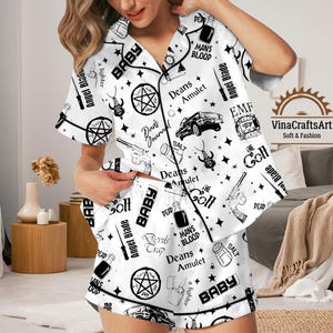 May include: White pajama set with a black pattern featuring text and illustrations. The set includes a short-sleeved button-up shirt and shorts. The design includes the words "BABY", "DEAD", "MANS BLOOD", and "Angel Blade".