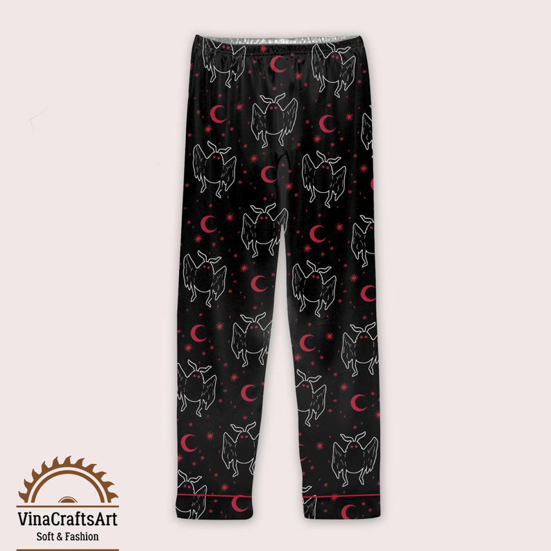 Op de afbeelding: Zwarte pyjamabroek met een herhalend patroon van witte vleermuisachtige wezens, rode halve manen en sterren. De broek heeft rode biezen en de tekst "VinaCraftsArt Soft & Fashion" aan de onderkant.