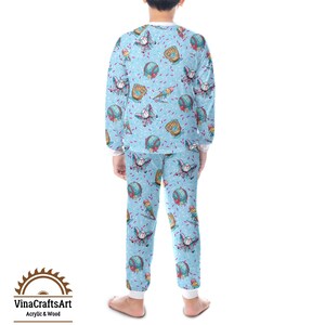 May include: Light blue pyjama set with a baseball theme. The long-sleeved top and trousers feature a repeating pattern of baseballs, gloves, and ice cream cones. The pyjamas have white cuffs and trim. The brand logo "VinaCraftsArt Acrylic & Wood" is visible.