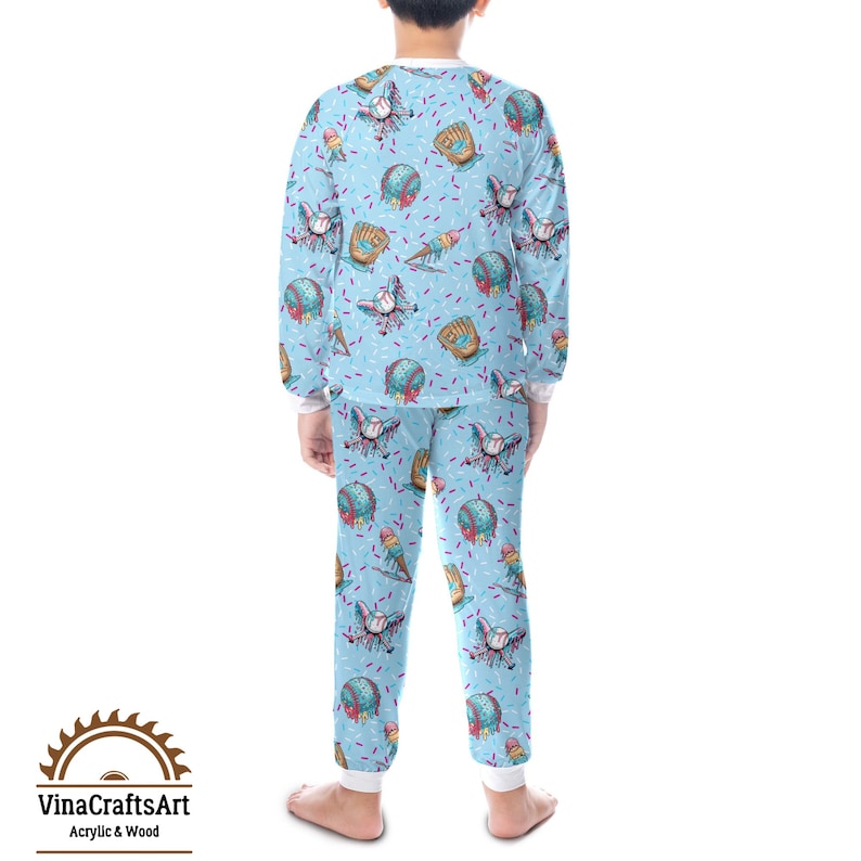 May include: Light blue pyjama set with a baseball theme. The long-sleeved top and trousers feature a repeating pattern of baseballs, gloves, and ice cream cones. The pyjamas have white cuffs and trim. The brand logo "VinaCraftsArt Acrylic & Wood" is visible.