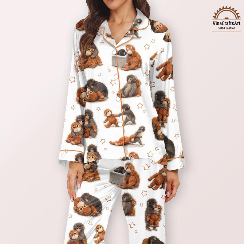 May include: White pyjama set featuring a repeating pattern of brown and grey monkeys and gold stars. The long-sleeved top and trousers have gold trim. The brand name "VinaCraftsArt" is visible in the upper right corner.