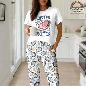 May include: White pajama set with an oyster graphic and the text "Moister Than An Oyster." The pajama pants feature an oyster and lemon pattern. The person is holding a white mug.