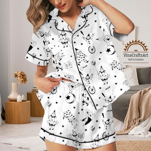 May include: White pajama set with a black circus-themed pattern. The short-sleeved top and shorts feature illustrations of clowns, stars, and balloons. The set is trimmed with black piping and has the text "VinaCraftsArt Soft & Fashion".