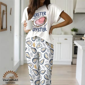 May include: A white pajama set with a short-sleeved top and pants. The top features the text "Moister Than An Oyster" with an oyster graphic. The pants have an oyster and leaf pattern. The set is soft and comfortable.