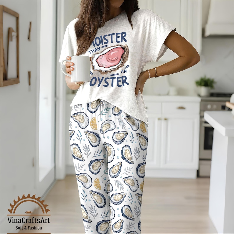 May include: A white pajama set with a short-sleeved top and pants. The top features the text "Moister Than An Oyster" with an oyster graphic. The pants have an oyster and leaf pattern. The set is soft and comfortable.