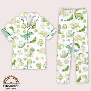 May include: White pajama set with a dinosaur pattern. The short-sleeved top and trousers feature green dinosaurs, eggs, and foliage. The set has black trim and is made of soft material.